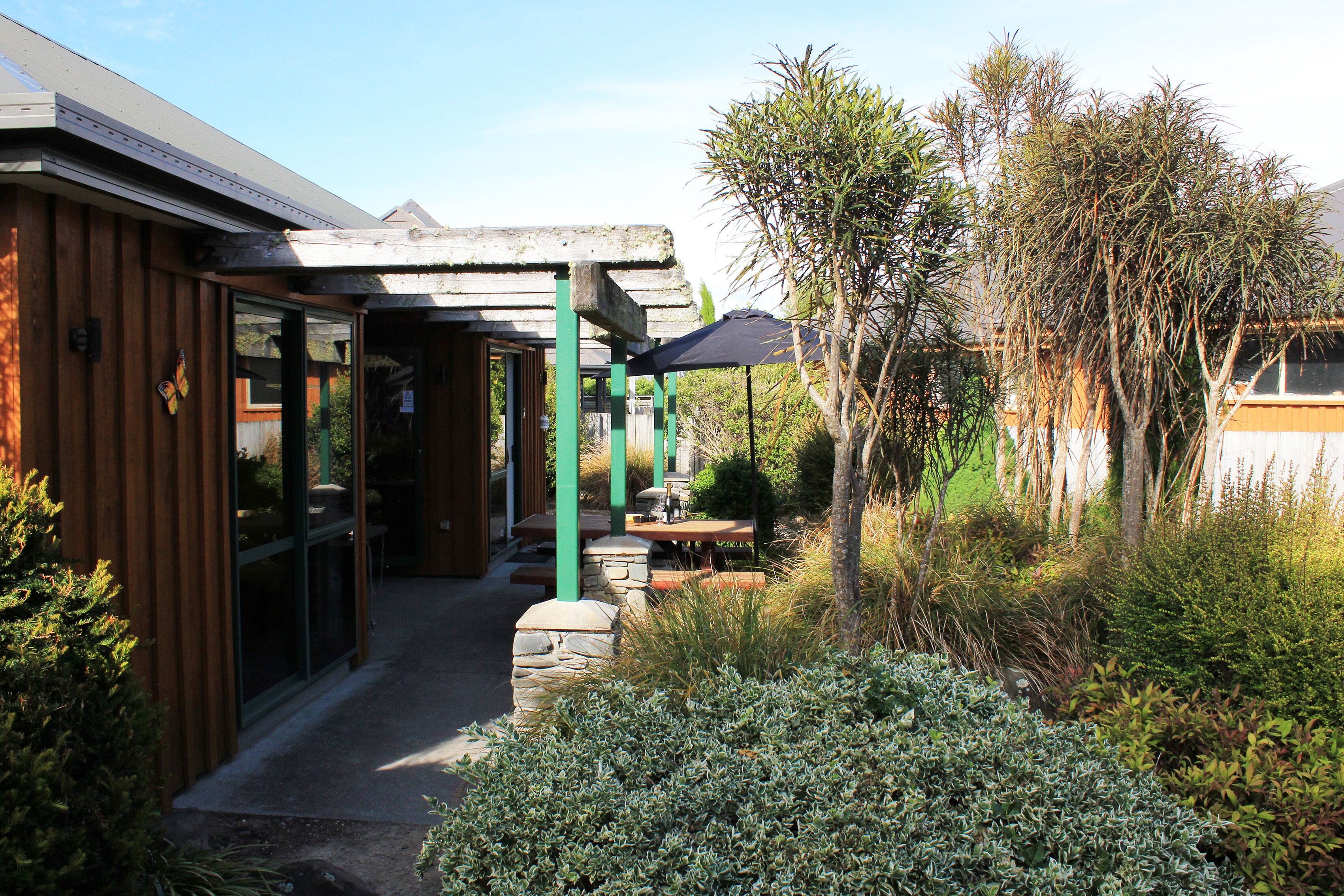 A wooden building with a covered outdoor seating area, stone steps, and a variety of plants.