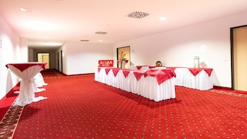 A hotel conference room with red carpet and white drapery, a sign reading "ACARA HOTEL", and a hallway in the background.