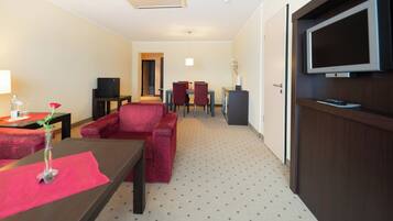 A hotel room with a sofa, a small table with a vase of flowers, a TV mounted on the wall, and a door.