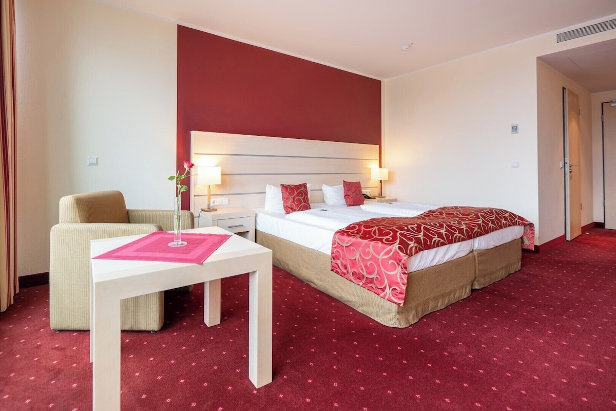 A hotel room with a bed, a chair, a table, and a nightstand.
