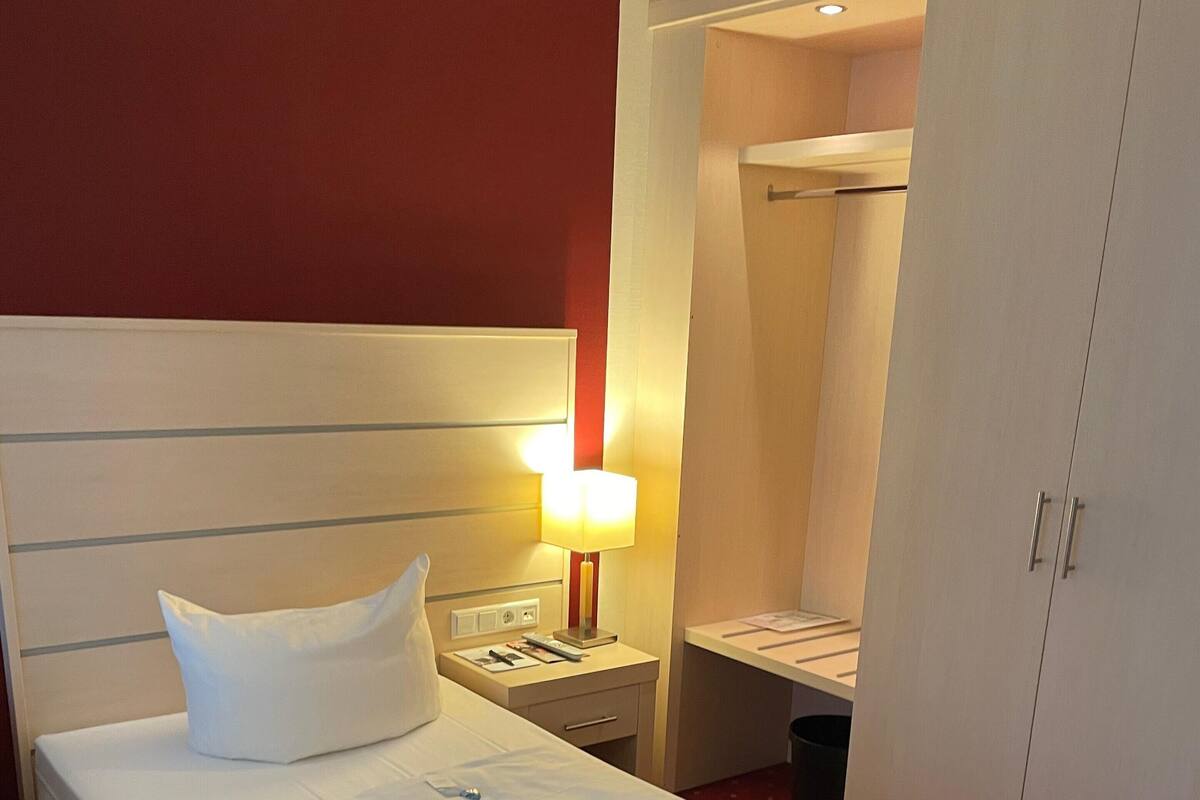 A hotel room with a bed, a nightstand, a lamp, a mirror, and a wardrobe.