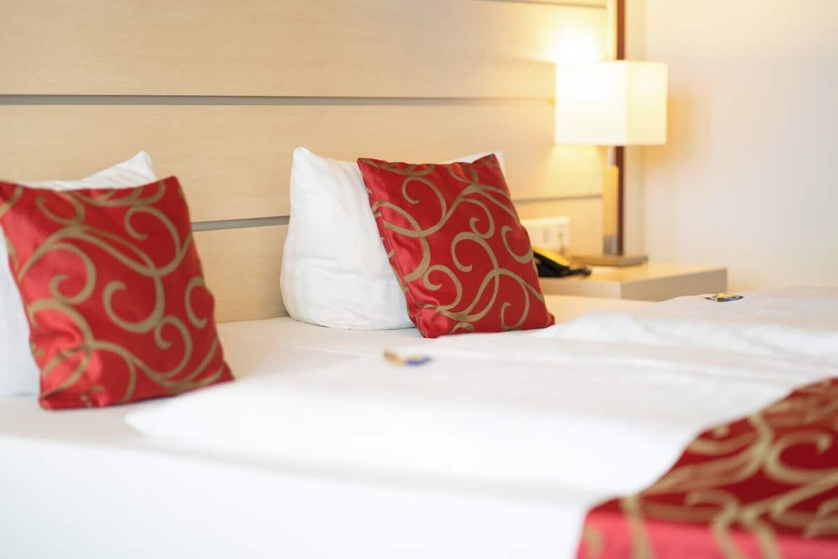 A hotel room with a neatly made bed, two pillows, a bedside table with a lamp, and a nightstand.