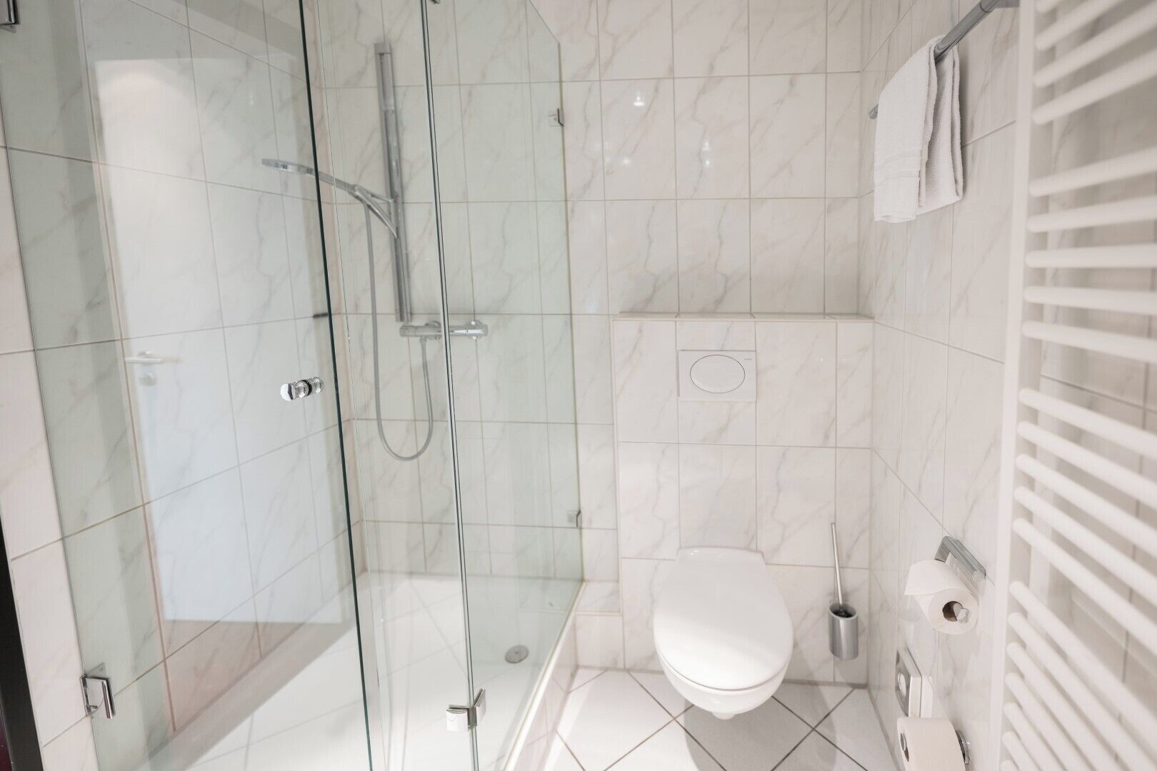 Ein modernes Badezimmer mit einer gläsernen Duschkabine, einer weißen Toilette und einem Handtuchhalter.