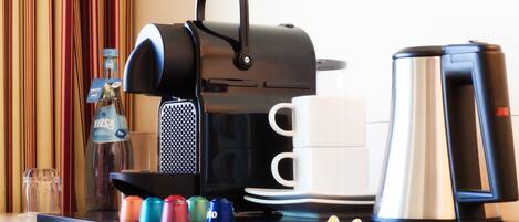 A coffee station with a coffee maker, a cup, a kettle, and a tray with colorful cans.