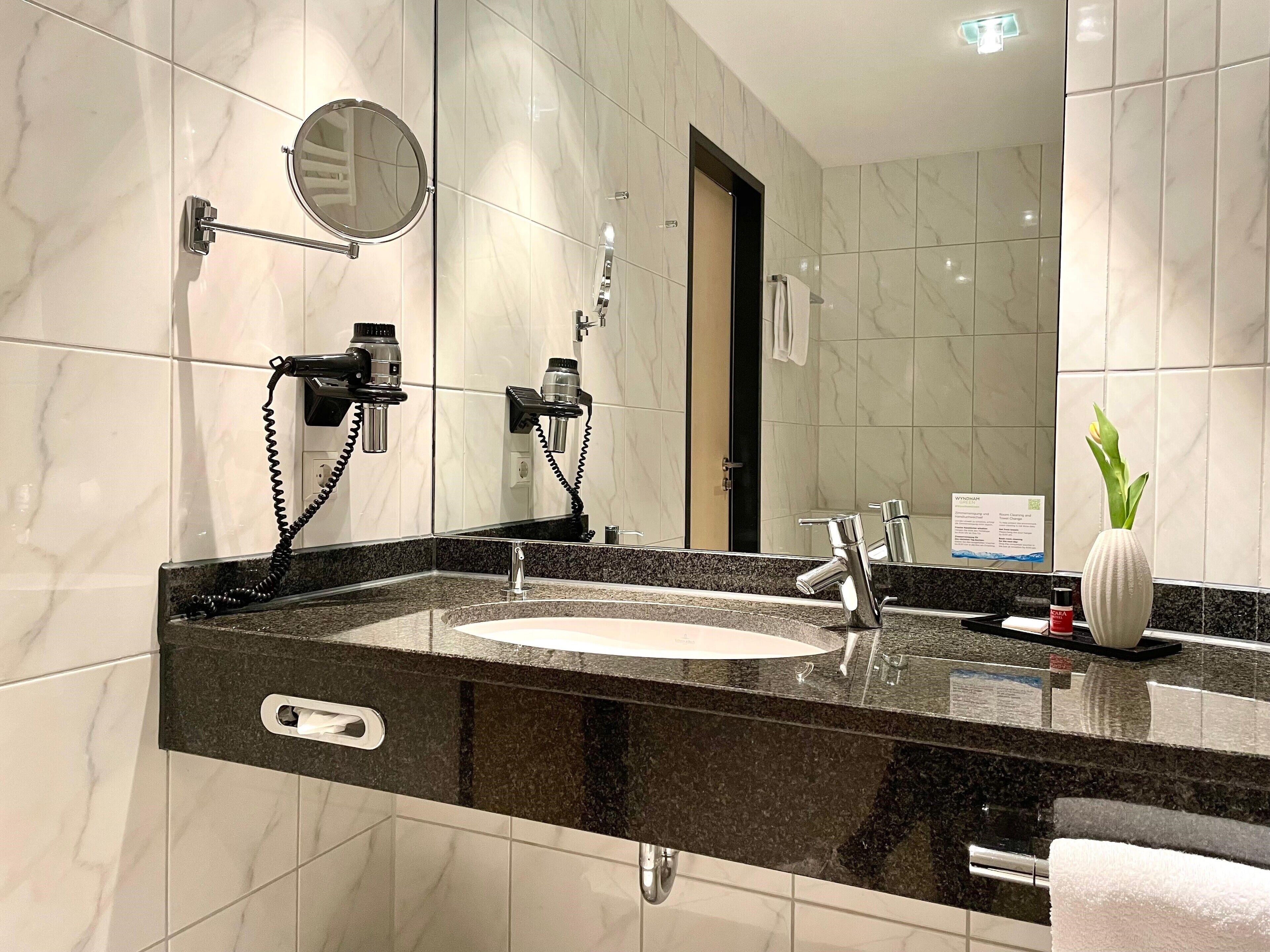 Un baño moderno con pared de azulejos de mármol, encimera de granito negro, lavabo con espejo y toallero.