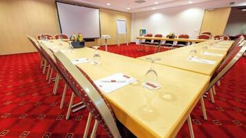 Ein Konferenzraum mit langem Tisch, Stühlen, einer Projektionsleinwand und einer Whiteboard.