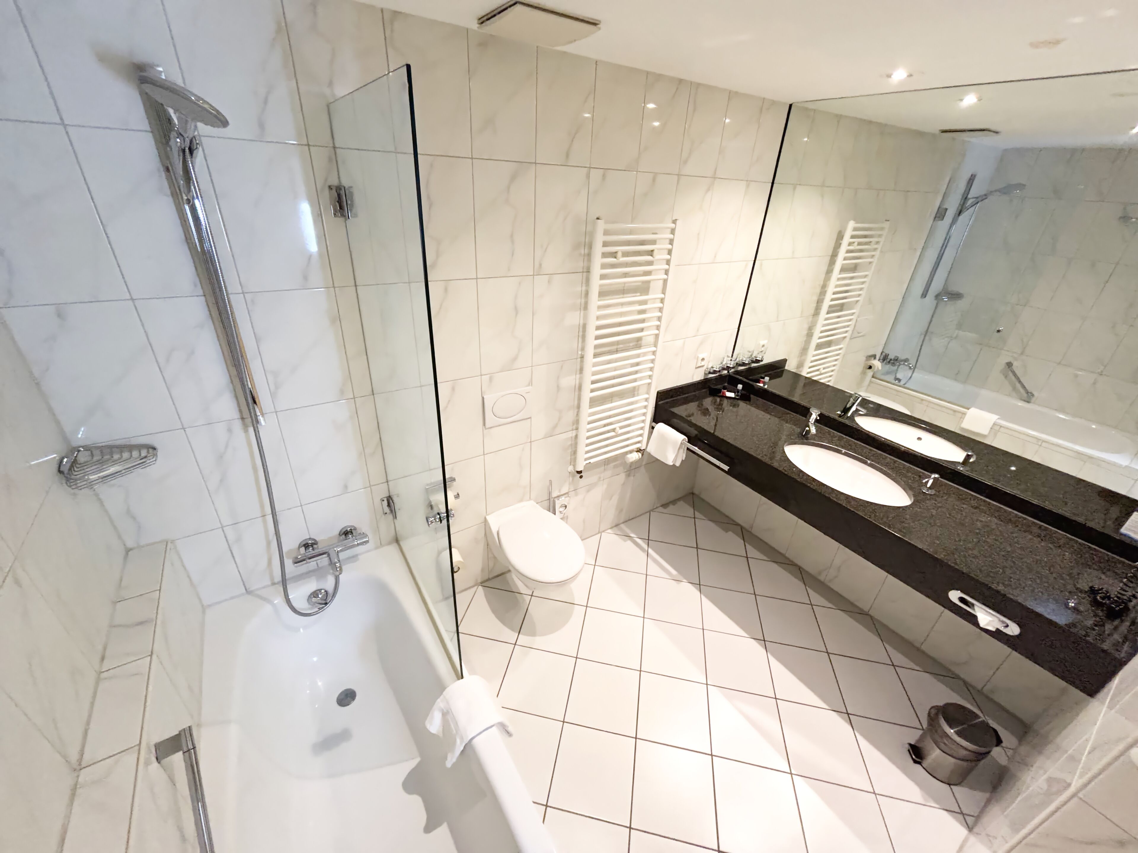 A modern bathroom with a glass-enclosed shower, a bathtub, and a vanity with two sinks.