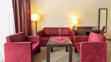 Ein Hotelzimmer mit einem roten Sofa, zwei roten Sesseln, einem kleinen Tisch mit Unterlage und zwei Nachttischlampen.