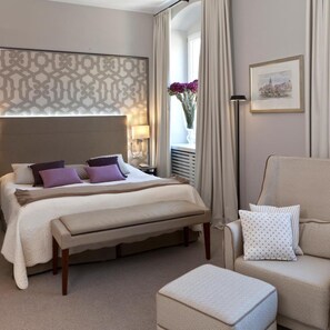 A hotel room with a large bed, a bedside table with a lamp, a chair, and a window with curtains.