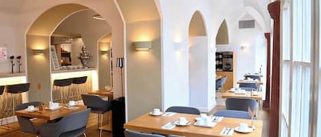 Un comedor moderno con varias mesas y sillas, techos abovedados y una zona de bar con mostrador.