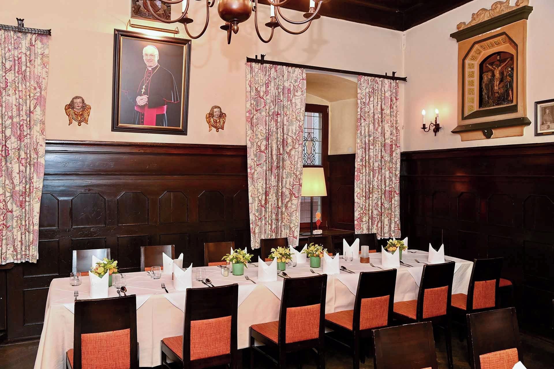 A dining area with a long table set for a meal, surrounded by chairs with orange cushions.