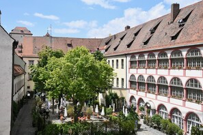 Ein Innenhof mit Außenbestuhlung, einem Baum und Gebäuden mit Rundbogenfenstern und einem Ziegeldach.