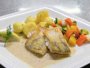Un plato con filetes de pescado, patatas hervidas y una ensalada de verduras variadas.