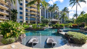 A resort with a large pool surrounded by palm trees and lounge chairs.