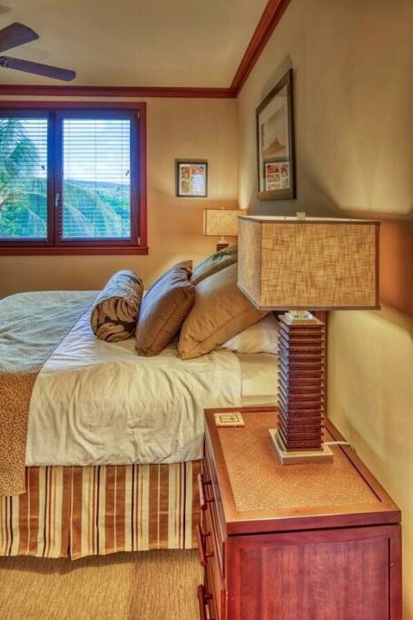Ein Schlafzimmer mit einem Bett, Kissen, einem Nachttisch, einer Lampe und einem Fenster mit Jalousien.