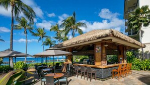 A beachside bar with a thatched roof, outdoor seating, and a view of the ocean.