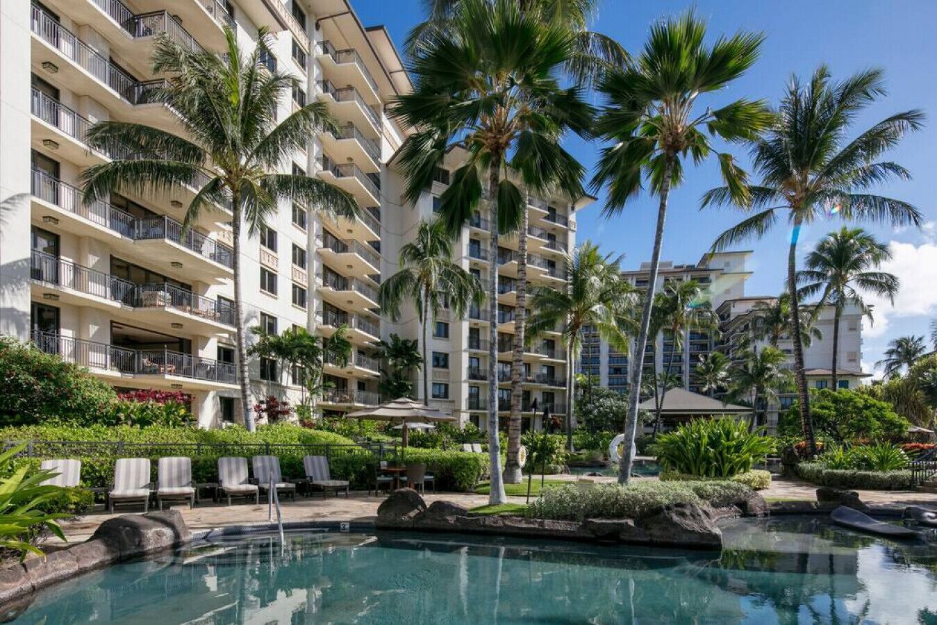 A hotel with multiple balconies, a swimming pool, and palm trees.