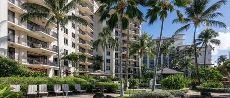 A hotel with multiple balconies, a swimming pool, and palm trees.