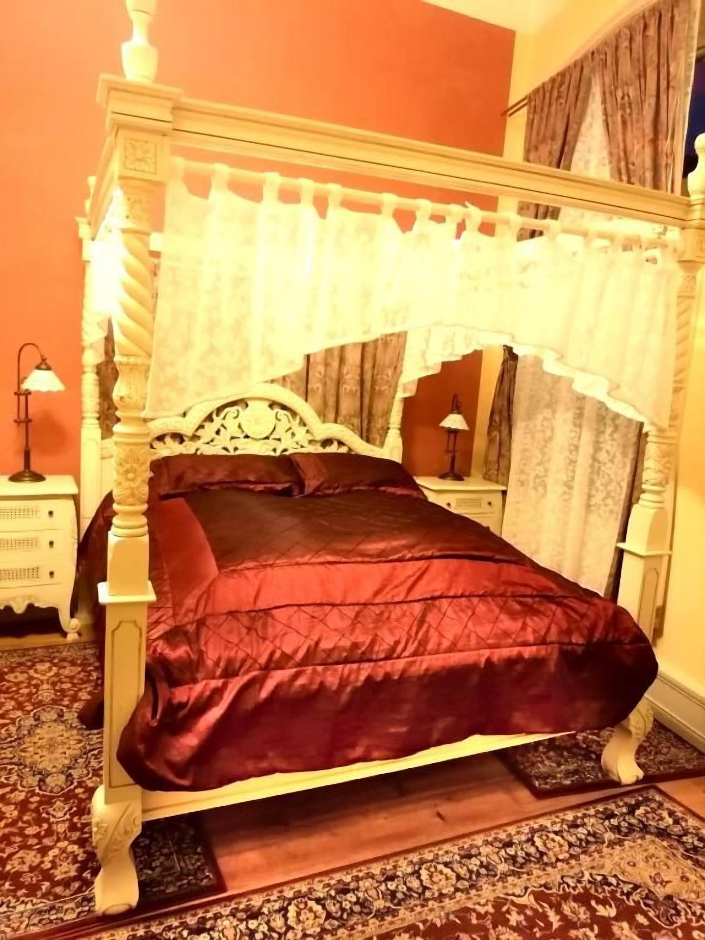 A four-poster bed with a dark red bedspread, a white canopy, and a wooden headboard.