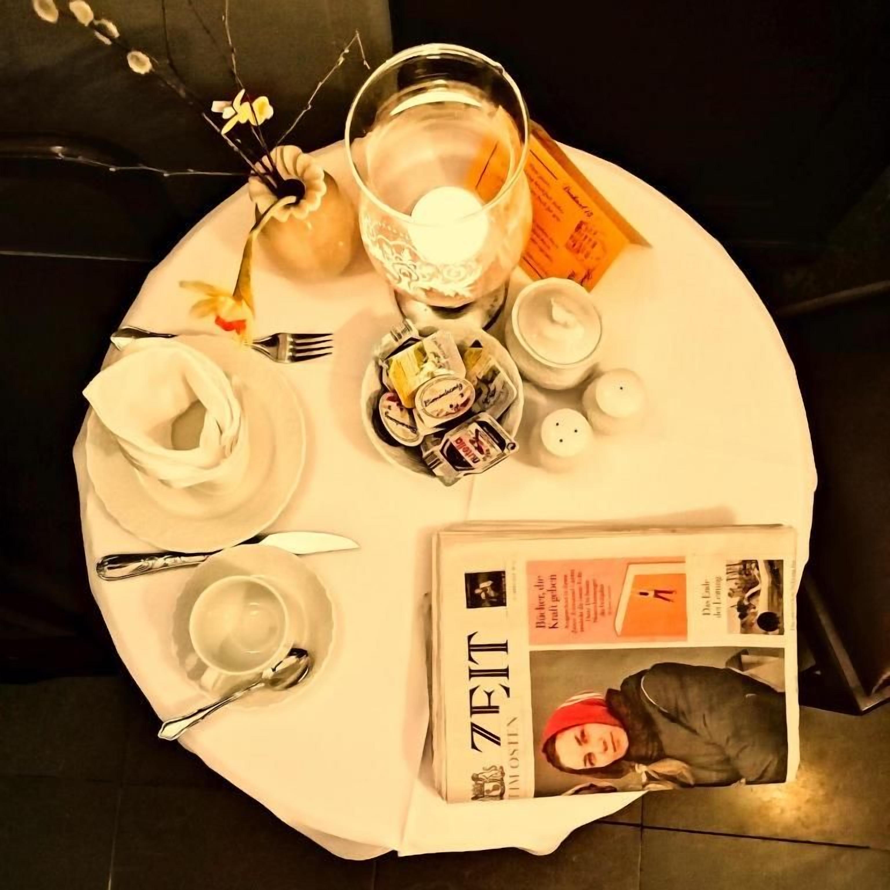 A round table with a newspaper, a glass with a candle, a tea set, and a menu.