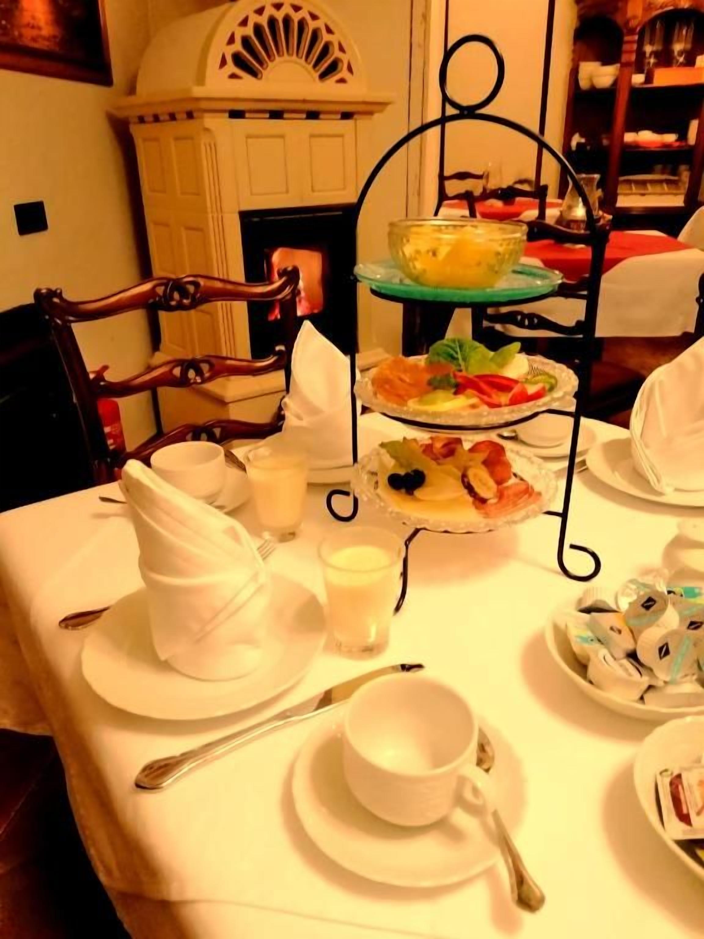 A dining table with a three-tiered dessert stand, white tableware, and a fireplace in the background.
