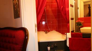 A bathroom with a red bathtub, a red chair, and a red curtain.
