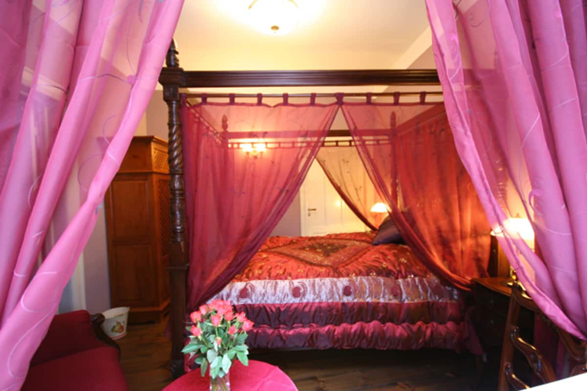 Ein Schlafzimmer mit einem Himmelbett, einem Holzschrank und einem Tisch mit Blumen in einer Vase.