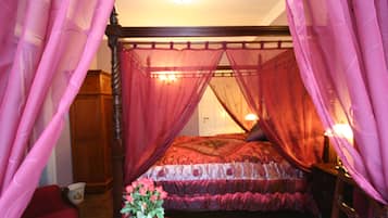 A bedroom with a four-poster bed, a wooden wardrobe, and a vase with flowers on a table.