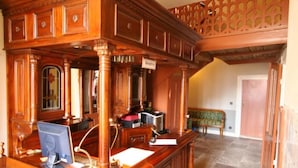 Habitación amplia con un escritorio de madera grande, una computadora y un teléfono. Se ve un banco al fondo y una escalera que sube a un nivel superior.