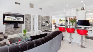 Un salon moderne avec un canapé gris, des fauteuils rouges, une table basse en verre et un téléviseur à écran plat fixé au mur.