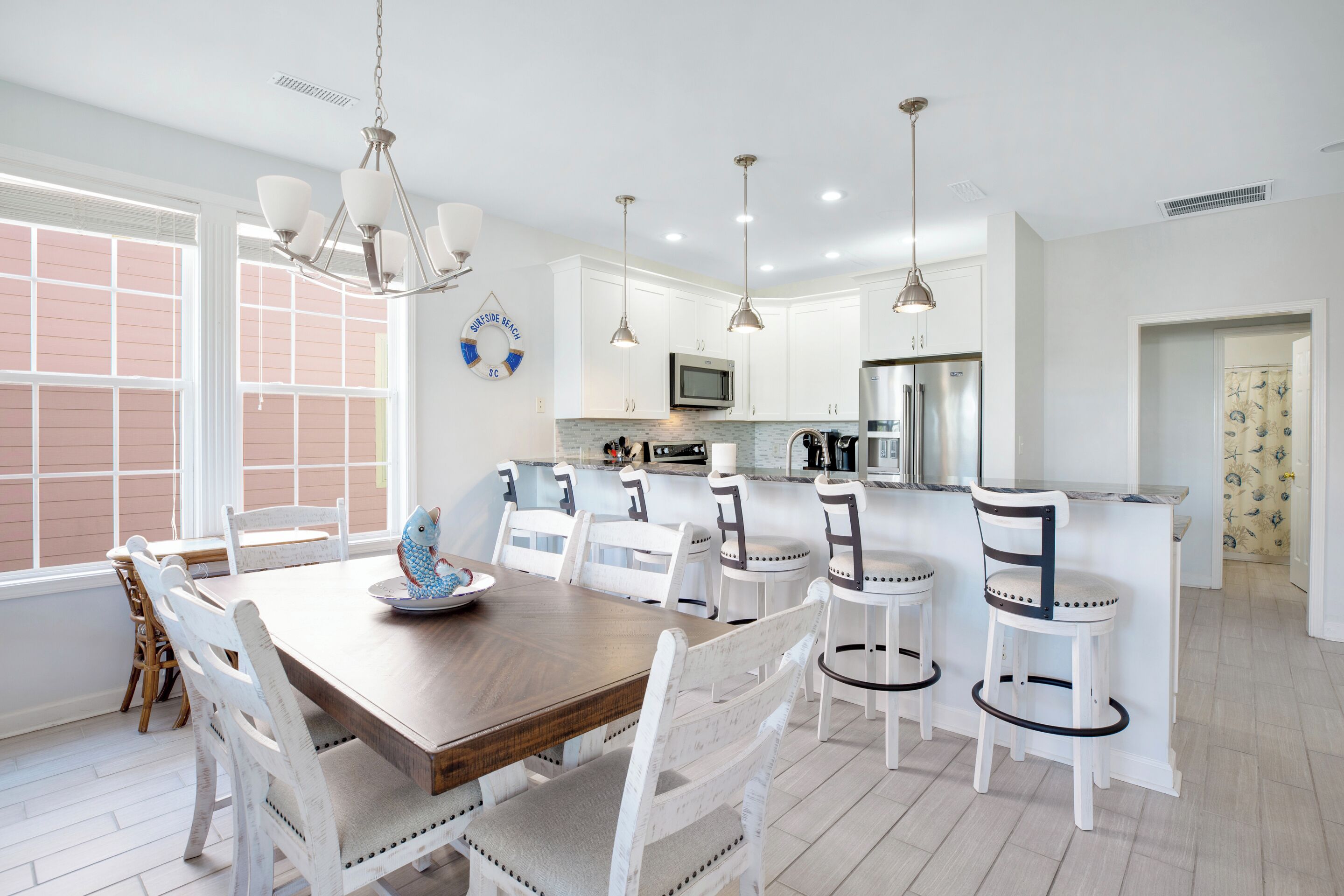 Une cuisine moderne avec des meubles blancs, des appareils en acier inoxydable et une table à manger en bois, assortie de chaises blanches.