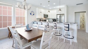Een moderne keuken met witte kasten, roestvrijstalen apparatuur en een houten eettafel met witte stoelen.