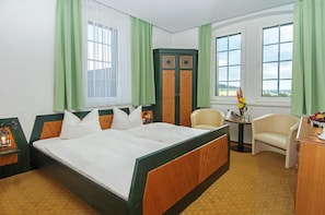 Quarto de hotel com uma cama grande, uma escrivaninha, uma cadeira e vista para o exterior.