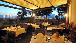 An outdoor dining area with tables set for two, each with a candle and a glass of water.