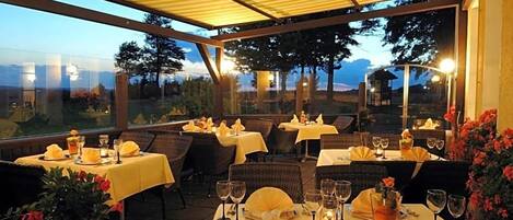An outdoor dining area with tables set for two, each with a candle and a glass of water.