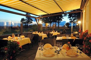 An outdoor dining area with tables set for two, each with a candle and a glass of water.