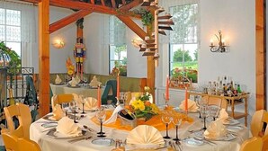 A dining area with round tables set for a meal, featuring white tablecloths, yellow chairs, and candle centerpieces.