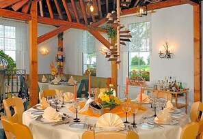 A dining area with round tables set for a meal, featuring white tablecloths, yellow chairs, and candle centerpieces.