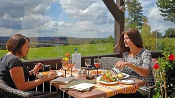 Two people dining at an outdoor table with a view of a green landscape.