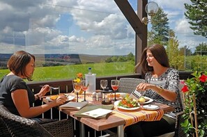 Two people dining at an outdoor table with a view of a green landscape.