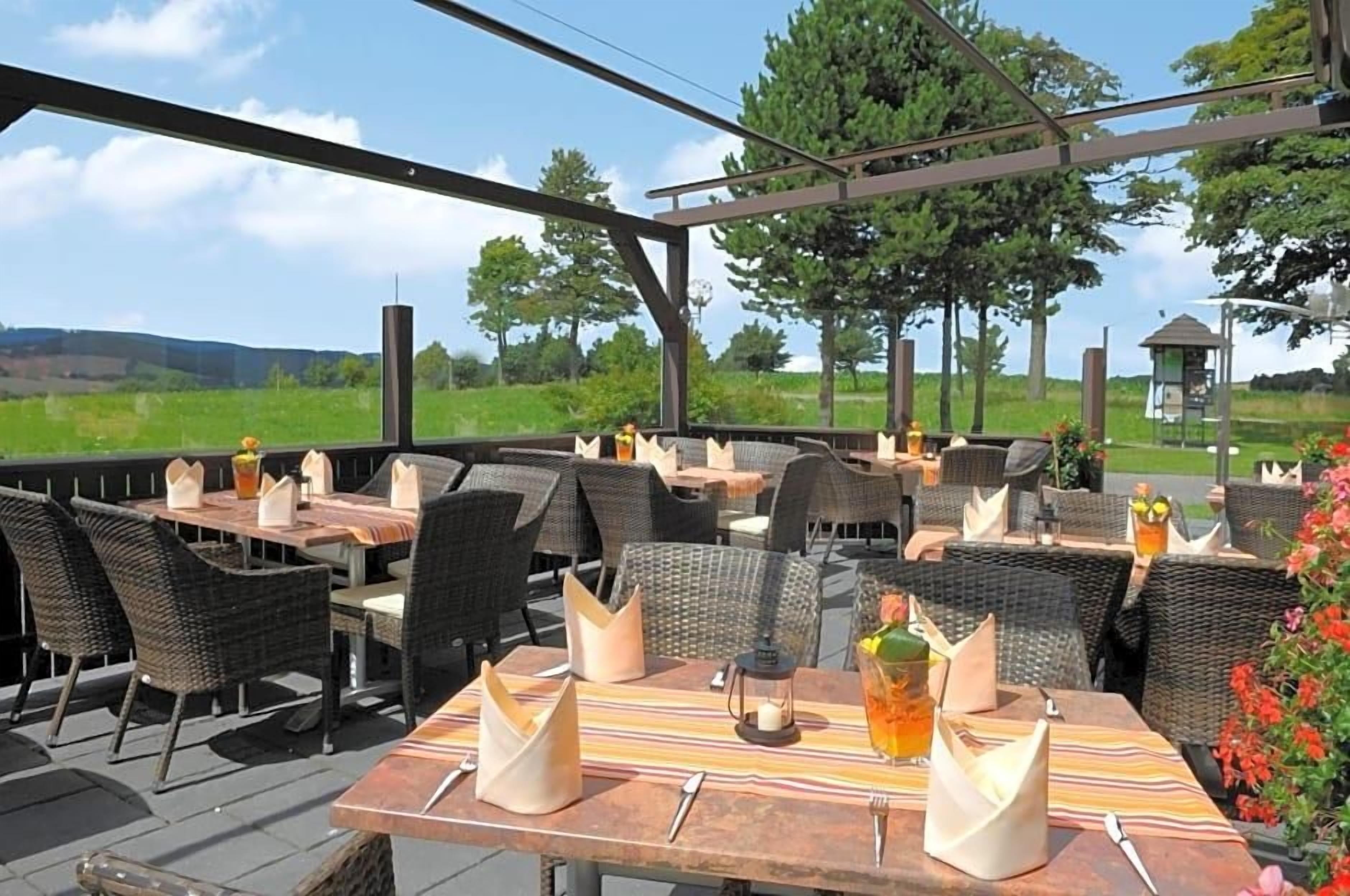 An outdoor dining area with wicker chairs and tables, a clear view of the landscape, and a gazebo in the background.