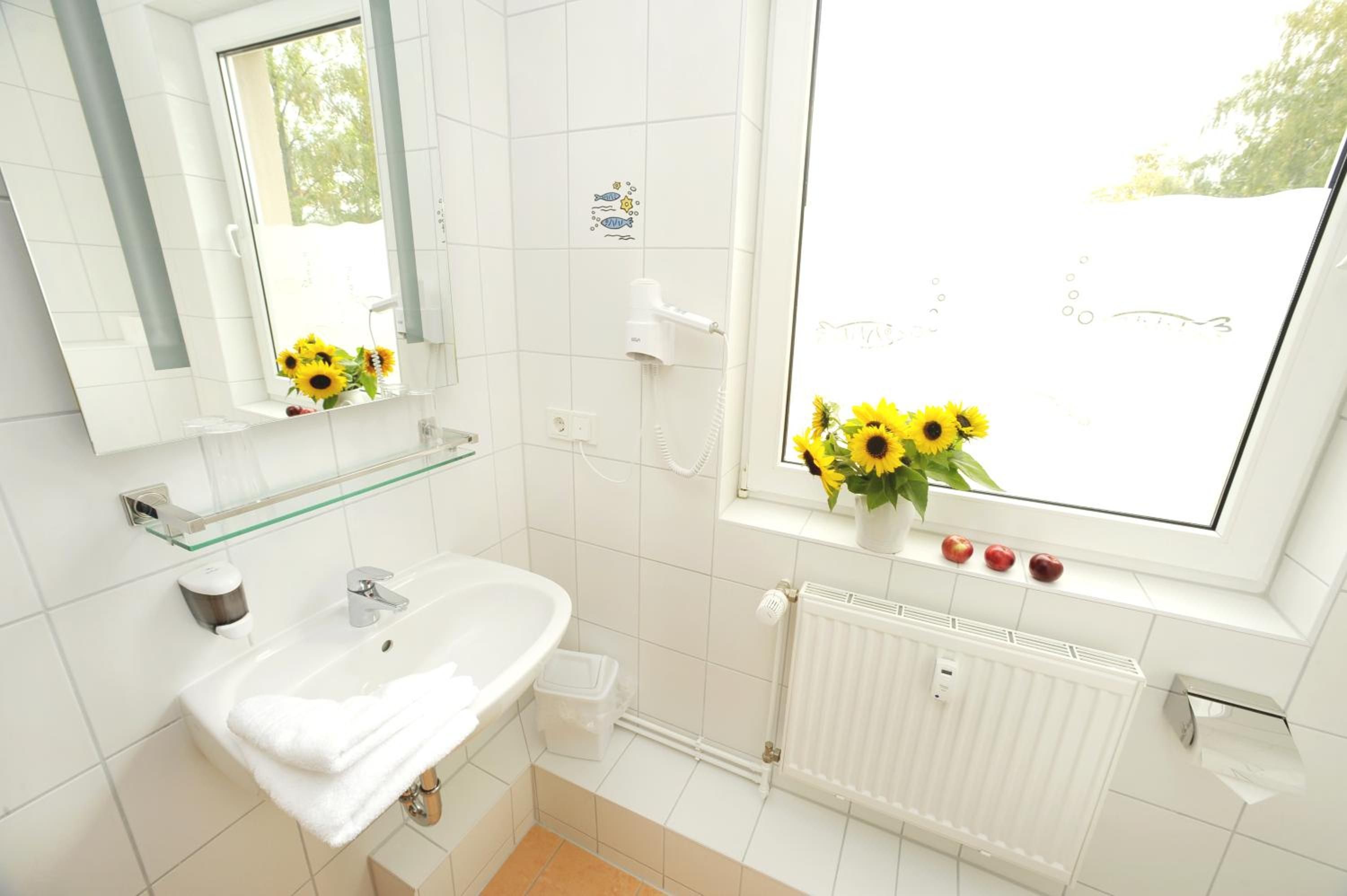 A bathroom with a white sink, mirror, and window with sunflowers.