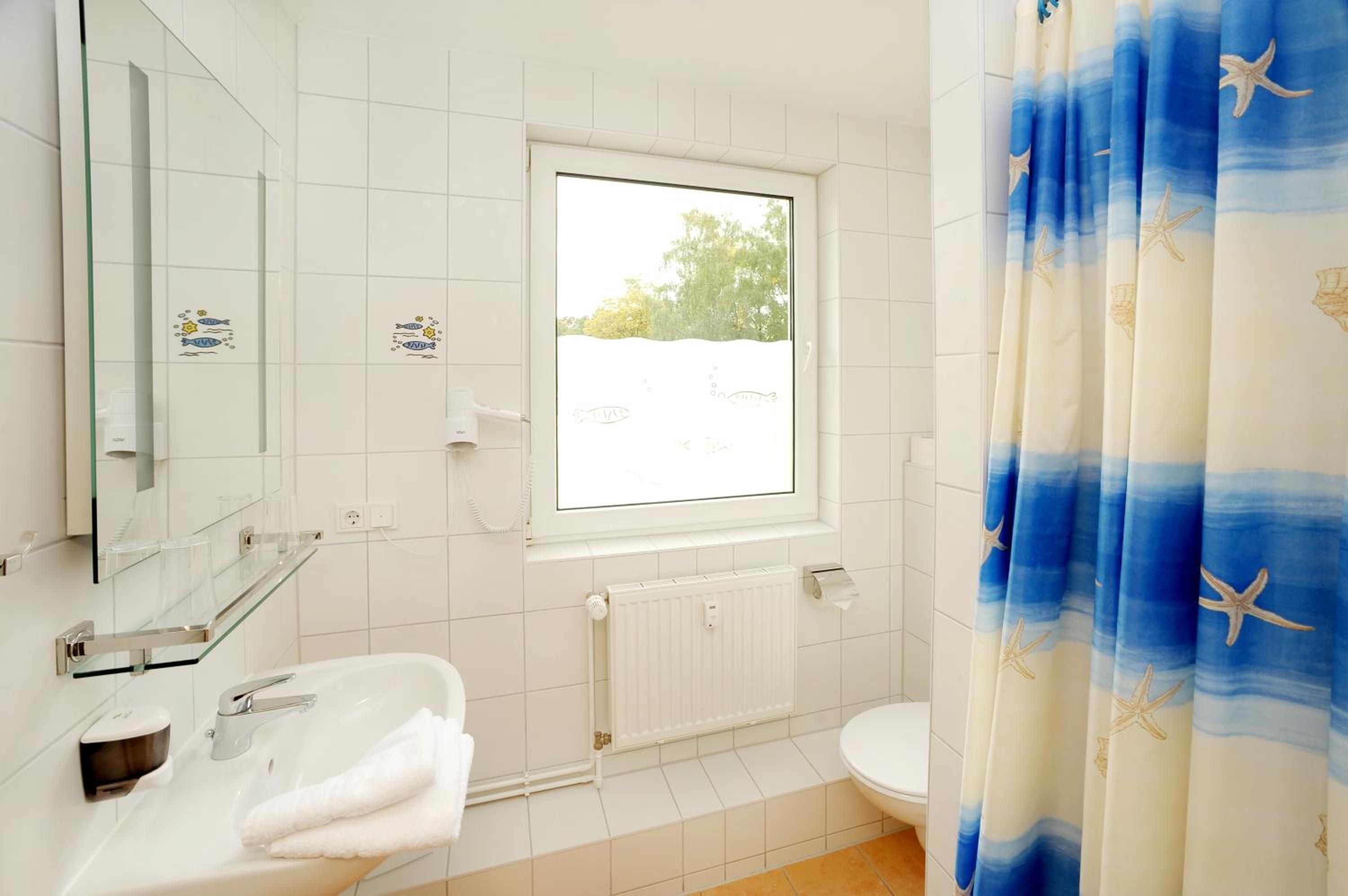 Et badeværelse med en hvid vask, et spejl, et vindue, et toilet og en bruseforhæng med stjernestjernedesign.