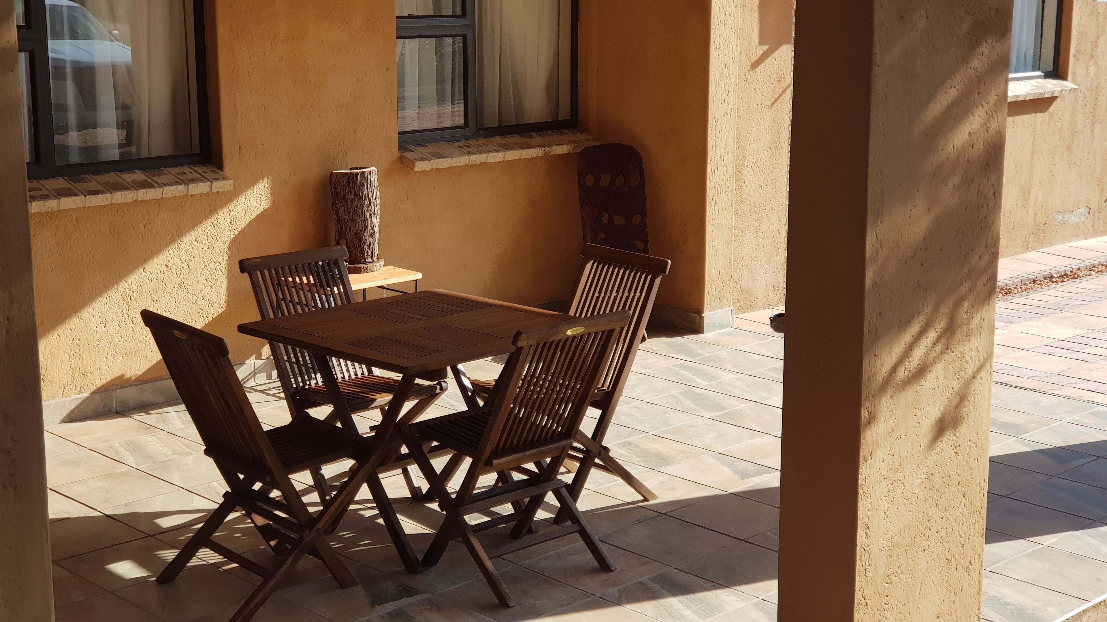 A patio with a wooden table and chairs, a vase, and a window with curtains.