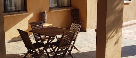 A patio with a wooden table and chairs, a vase, and a window with curtains.