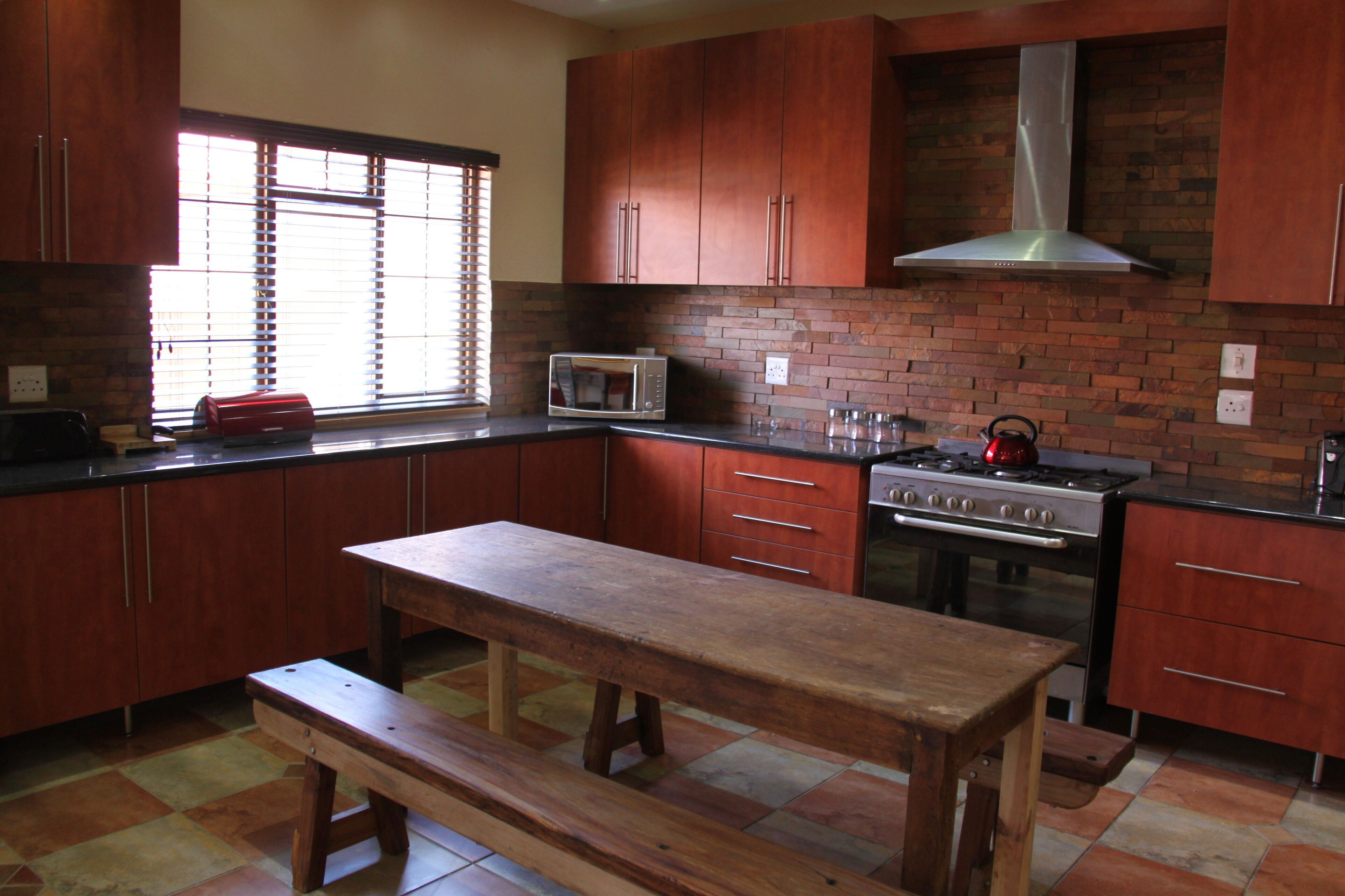 Una cocina con armarios de madera, salpicadero de ladrillo, un banco de madera, un microondas y una estufa.