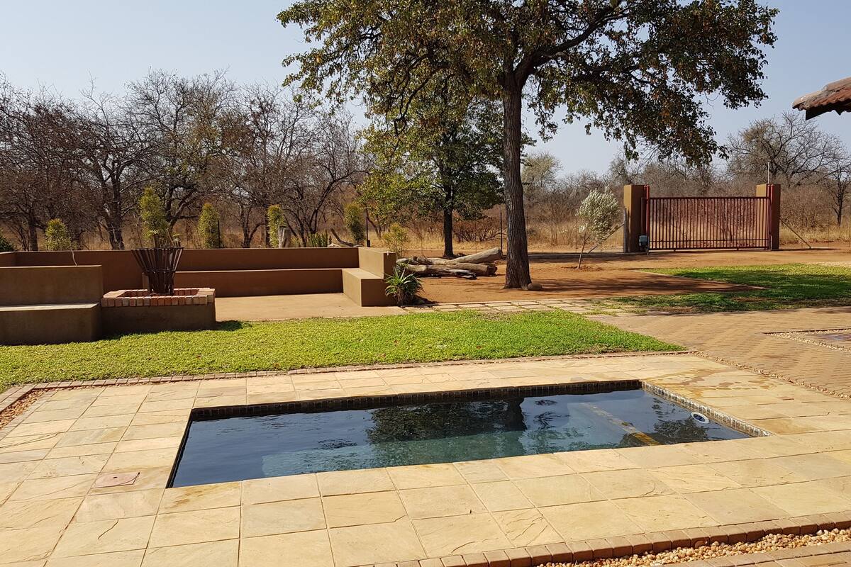 A swimming pool with a stone deck, surrounded by a grassy area and trees.