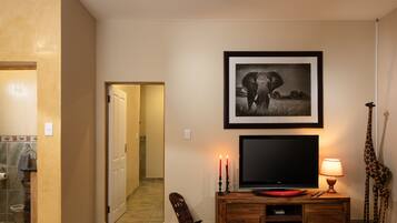 A living room with a television, a framed picture of an elephant, a lamp, and a giraffe statue.