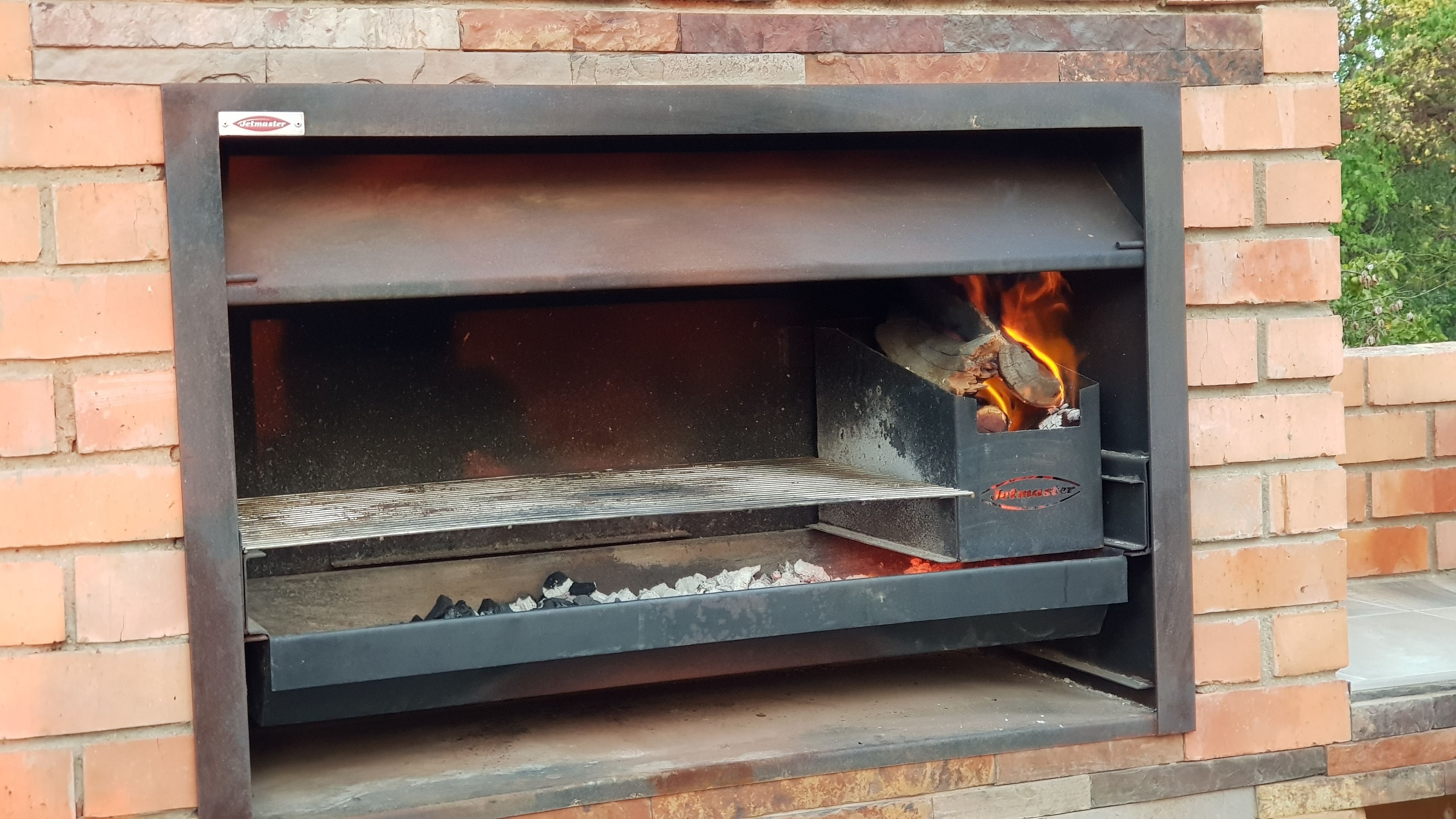 Un four en briques avec une porte en métal, une étagère en métal et un feu visible à l’intérieur.