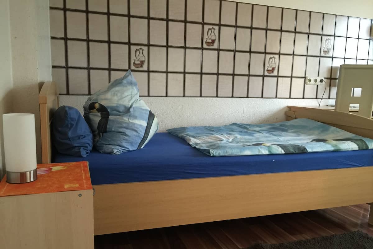 A bed with a blue mattress, pillows, and a bedside table with a lamp.